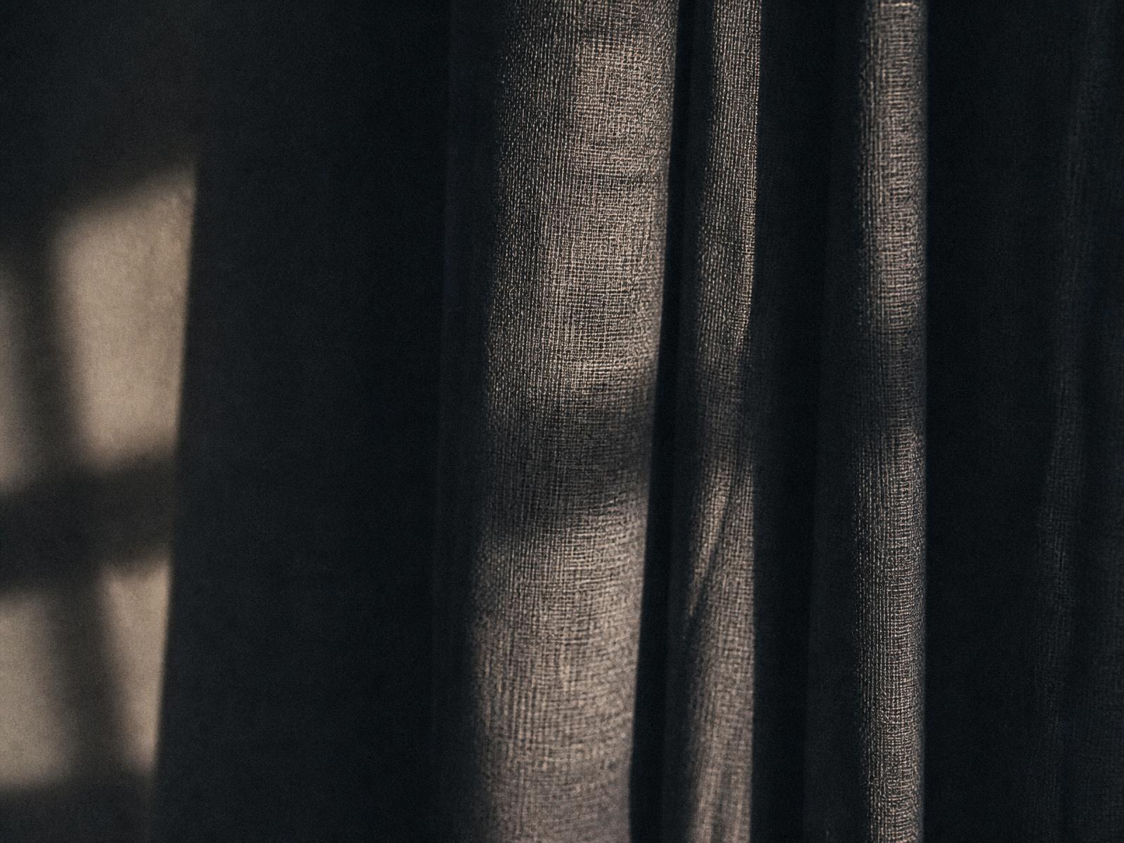 Dark curtain folds lit by a thin edge of window light